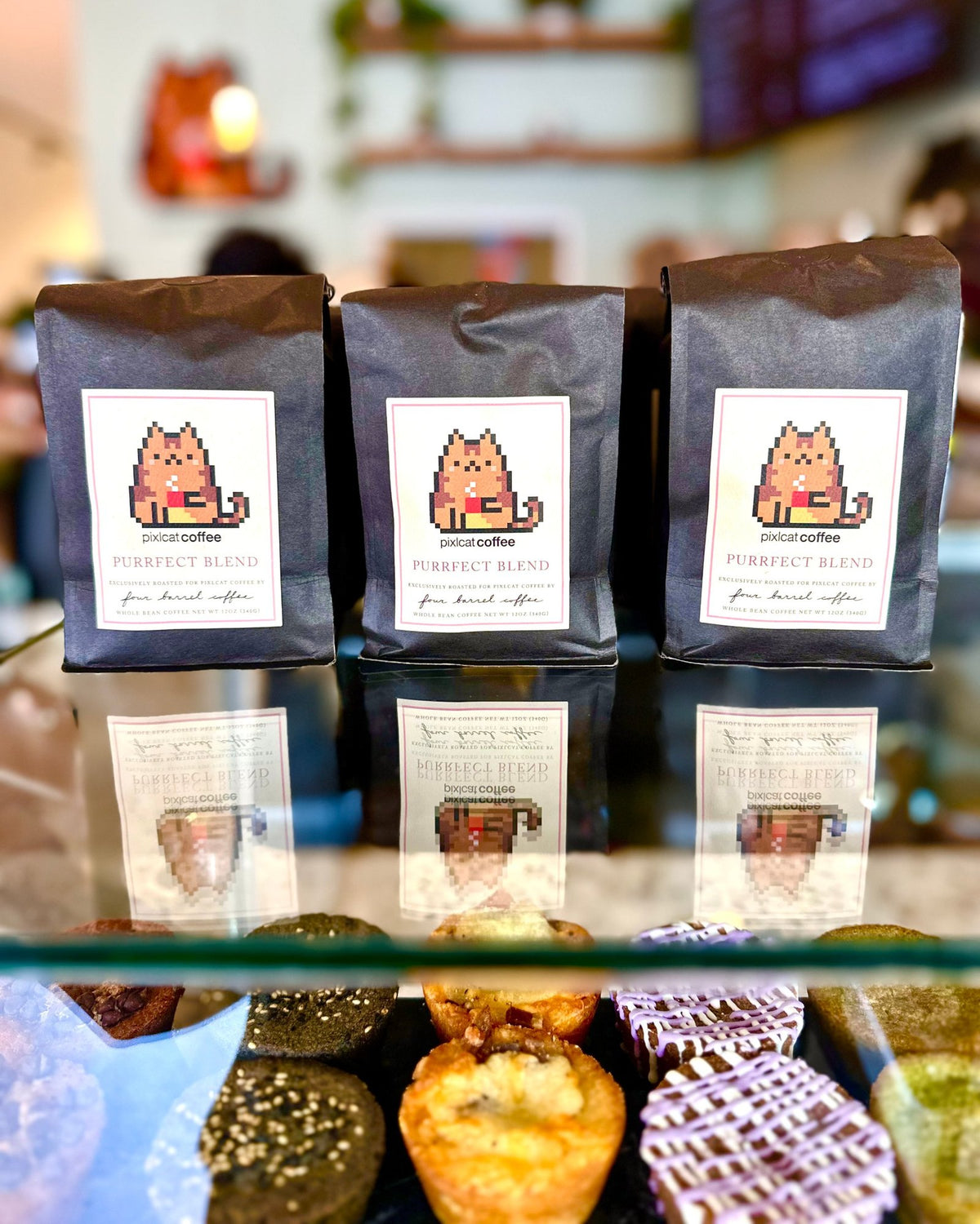 Three bags of Pixlcat Purrfect Blend coffee by Four Barrel Coffee on the café counter above a case of butter mochi